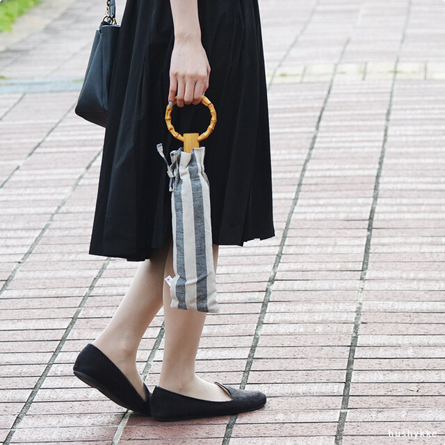 こちらの日傘は、コンパクトに収納できる、二つ折の折りたたみタイプ。持ち手分と石突き部分には天然の竹を、留め具はスナップボタンを使用しています。折りたたみタイプは、生地の耳を使用しないベーシックなデザイン。たたんだ際には、持ち手の溝にカサの骨がしっかり収納できるなど、細部にまでこだわって作られています。こちらの持ち手も輪っかになっているので、コンパクトに腕に通せて荷物が多いときも嬉しいですね。