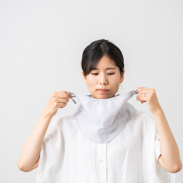 首元にセットしたマスクの上部を両手で持ち、顔のラインに沿って優しく上へ引き上げます。