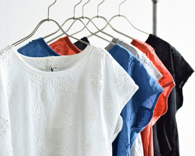 立体的なフラワーレース刺繍が華やかで涼しげな印象のブラウスは、手前からオフホワイト、ブルー、グレイ、オレンジ、ブラックの5カラー展開。どれも夏のおでかけコーデに大人らしさを添える、上品な一枚です。